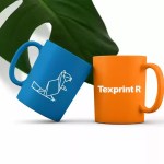 A blue mug with a white geometric beaver logo and an orange mug featuring the TexPrint R brand text, displayed in front of a tropical leaf.