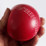 Hand squeezing a red soft PU foam cricket ball demonstrating its soft material.