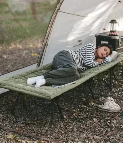 Nature hike explorer carrying a rolled-up foldable camping mattress toward a basecamp setup.