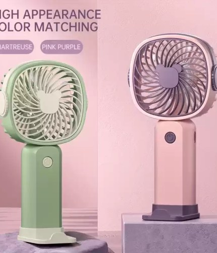 1800mAh mini portable fan in white shown held in a hand with a blurred forest background.