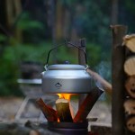 Pure aluminum camping kettle sitting on a rock next to a hiking rucksack during a nature hike.