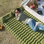Woman lying on green inflatable camping sleeping mat outside tent