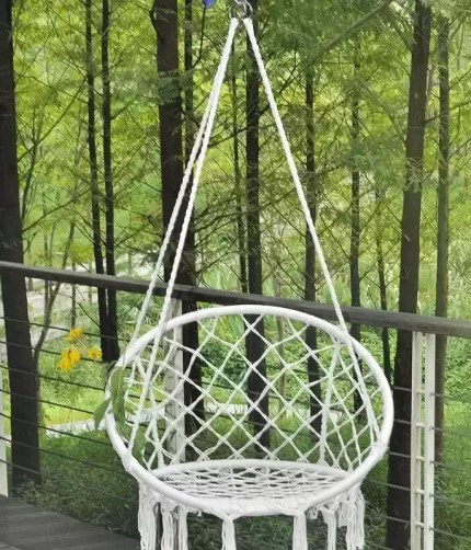 A woman relaxing in the woven hanging basket swing on a modern balcony.