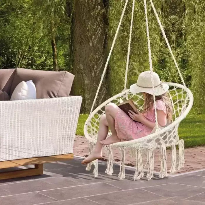 Hand-woven cotton rope hanging chair in a natural cream color suspended in a garden.