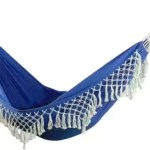 Blue double enlarged canvas hammock with retro tassels hanging between two trees.