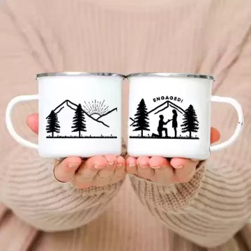 Two personalized engaged couple camp mugs with a creative woods print sitting on a wooden log.