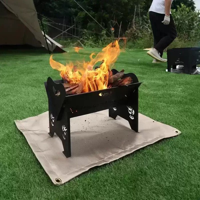Portable fire blanket spread out on green grass under a burning metal fire pit to prevent scorching.