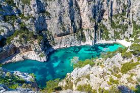 Aerial view of a turquoise lagoon surrounded by rugged cliffs and lush greenery in Calanques National Park, France.