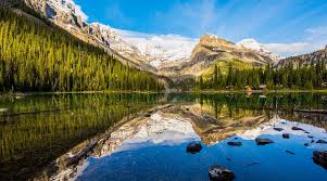 Scenic view of a mountain range reflecting in a tranquil lake surrounded by lush greenery.