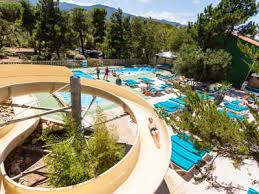 Aerial view of a waterslide spiraling down into a swimming pool area surrounded by lounge chairs and trees.