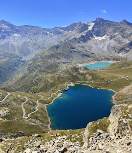 A panoramic view of a mountainous landscape featuring glacial lakes and winding roads, showcasing the dramatic beauty of nature.