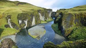 A stunning landscape of Fjaðrárgljúfur Canyon in Iceland, featuring steep, moss-covered cliffs and a winding river flowing through the canyon.