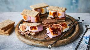 A close-up of s'mores made with graham crackers, roasted marshmallows, and chocolate bars, arranged on a wooden platter.