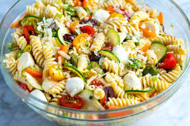 A colorful bowl of cold pasta salad with fusilli pasta, cherry tomatoes, cucumber, olives, and feta cheese, all tossed together with Italian dressing.