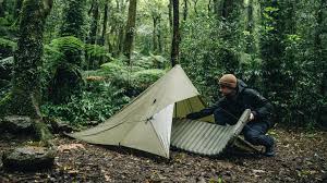 A person setting up a tent in a dense forest, surrounded by greenery.