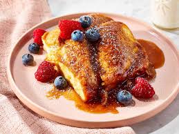 A plate of French toast topped with fresh raspberries and blueberries, drizzled with syrup.