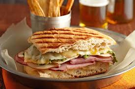 A grilled sandwich or panini made with layers of cheese, deli meats, and greens, served with a side of crispy fries.