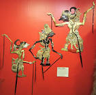 Three traditional Indonesian shadow puppets displayed against a red background.