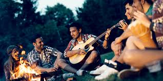 A group of friends enjoying a campfire while one person plays the guitar, creating a cozy outdoor atmosphere.