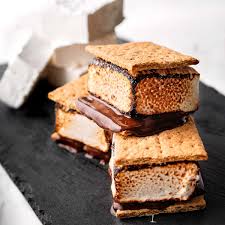 A close-up image of stacked s'mores, consisting of crispy graham crackers, melted chocolate, and toasted marshmallows, set against a dark surface.