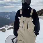Snowboarder wearing beige bib trousers and a black jacket on a snowy mountain