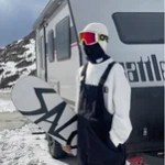 Side view of black insulated snowboard bib trousers beside a mountain vehicle