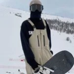 Snowboarder wearing beige waterproof bib trousers while carrying a snowboard