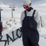 Snowboarder wearing black waterproof bib trousers on a snowy mountain slope