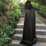 Long black hooded witch cape worn outdoors for Halloween costume use