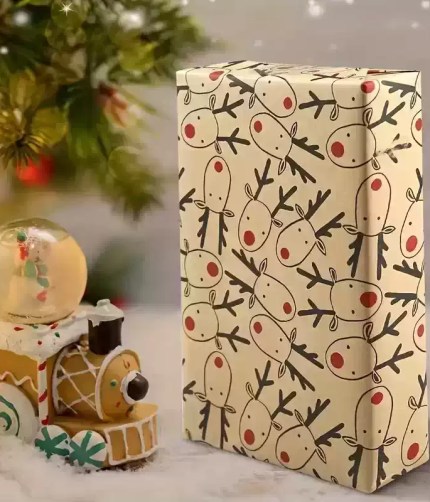 Gift box wrapped in reindeer paper beside toy train ornament.