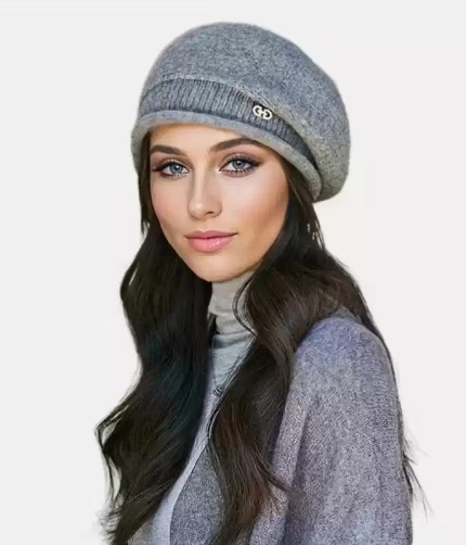 Grey knitted slouchy beanie hat featuring a ribbed band and a small metallic logo detail worn by a model.