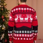A man and woman wearing matching red and black Christmas reindeer knit sweaters near a decorated tree.