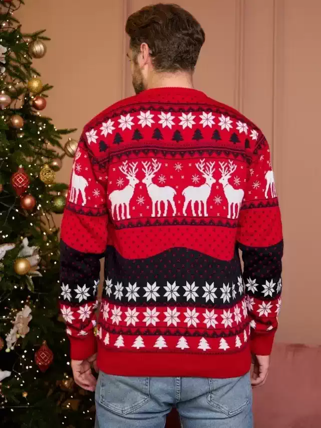 CHRISTMAS REINDEER SWEATER UK_1 A man and woman wearing matching red and black Christmas reindeer knit sweaters near a decorated tree.