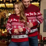 Couple wearing matching red knit Christmas sweaters with reindeer patterns.