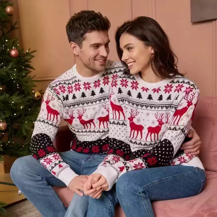 Man and woman sitting together on a pink sofa in matching white and red fair isle Christmas sweaters with reindeer patterns.