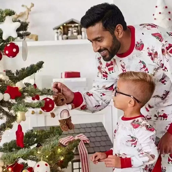Father and child wearing matching Christmas pyjamas while decorating the tree