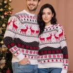 Man and woman standing side-by-side in matching white, red, and black reindeer Christmas sweaters.