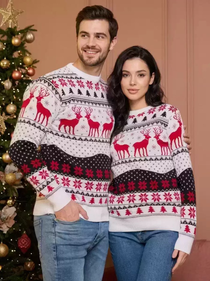 Man and woman standing side-by-side in matching white, red, and black reindeer Christmas sweaters.