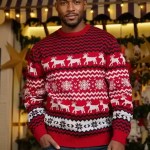 Man posing in a red and white knit Christmas sweater with reindeer and snowflake details