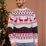 Man standing in front of a Christmas tree wearing a white knit Christmas sweater with red reindeer and snowflake details.