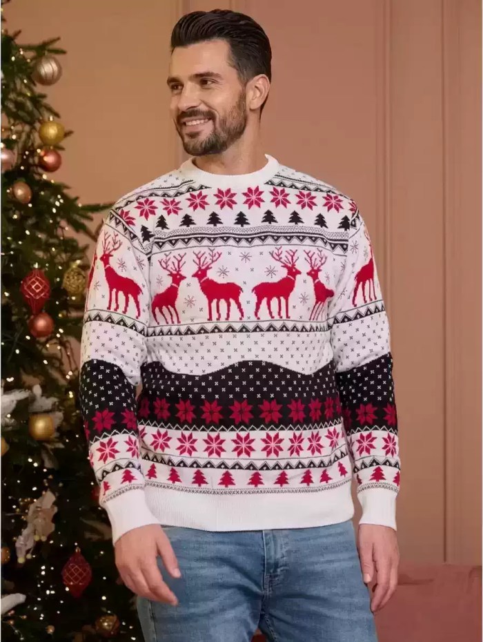 Man standing in front of a Christmas tree wearing a white knit Christmas sweater with red reindeer and snowflake details.
