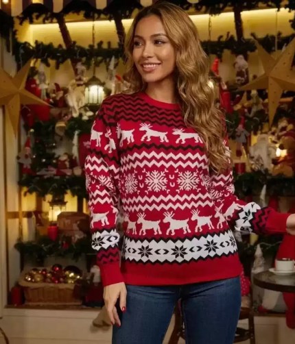 Woman smiling while wearing a red knit Christmas sweater with white reindeer patterns.
