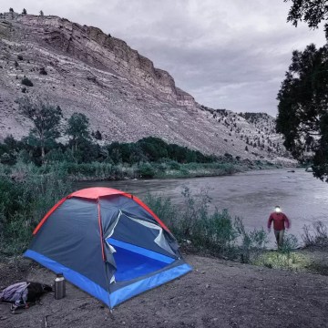 Compact dome camping tent pitched by riverside, ideal for UK wild camping and hiking trips