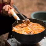 Titanium grill clip flipping meat on a portable BBQ during a UK wilderness camp.