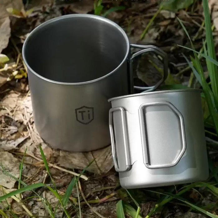 Compact titanium cup with folding butterfly handles designed to nest around a standard UK gas canister.
