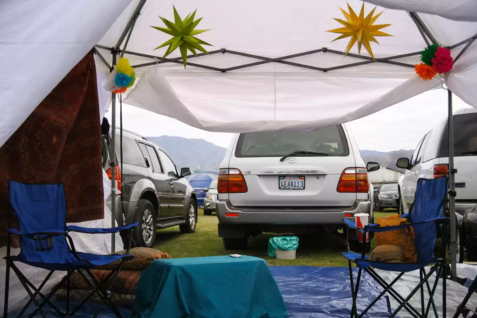 Interior view of a car camping canopy setup with folding chairs, table, decorations, and parked SUV creating a shaded outdoor living area at a campsite