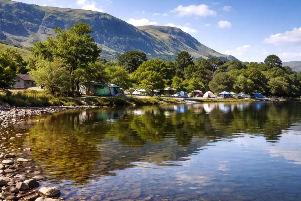 Tents set along lakeshore with clear water reflection and mountains in background, peaceful Lake District campsite setting in UK