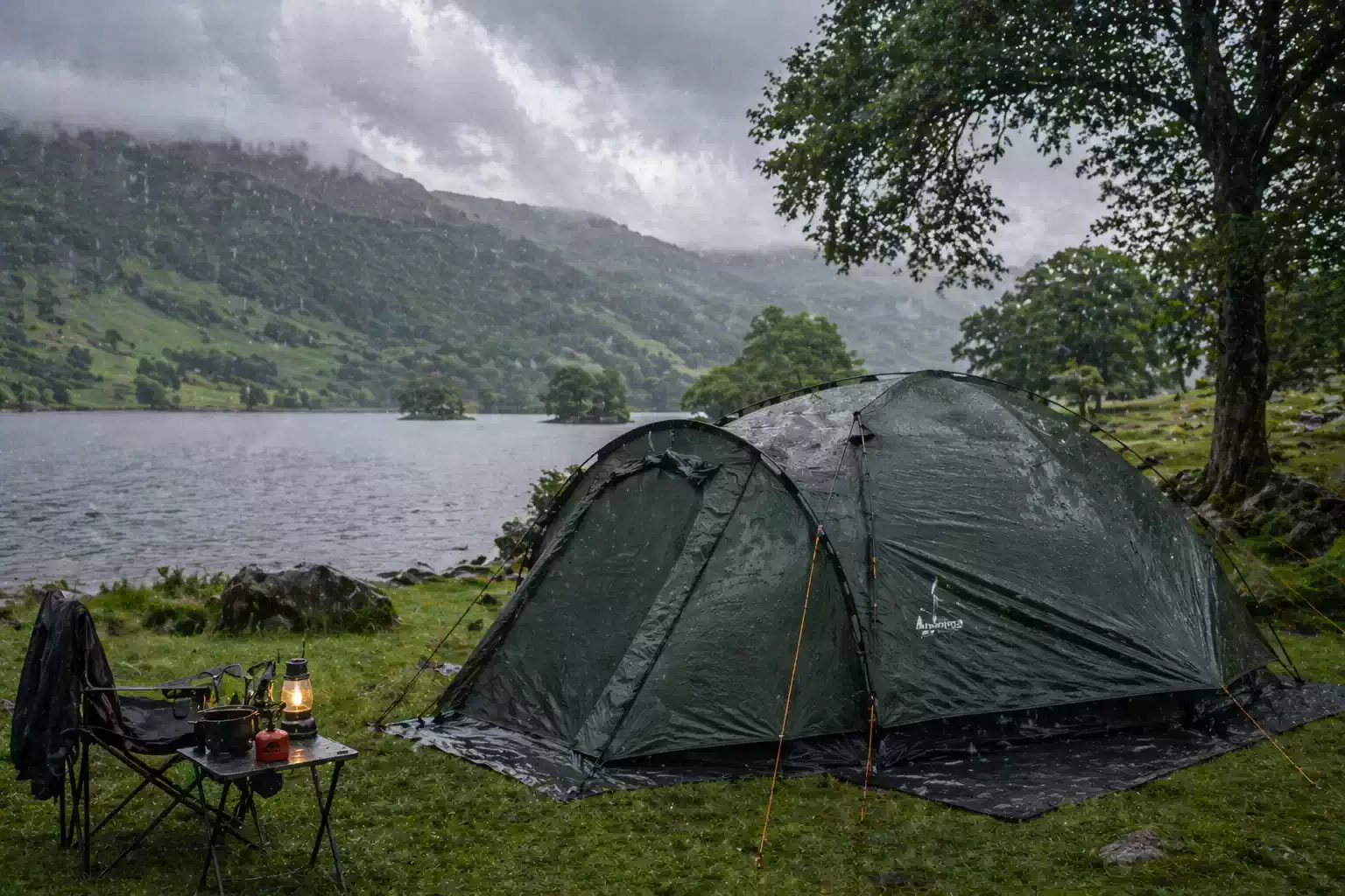 Waterproof tent pitched by Ullswater lake in rainy weather with camping lantern and gear setup