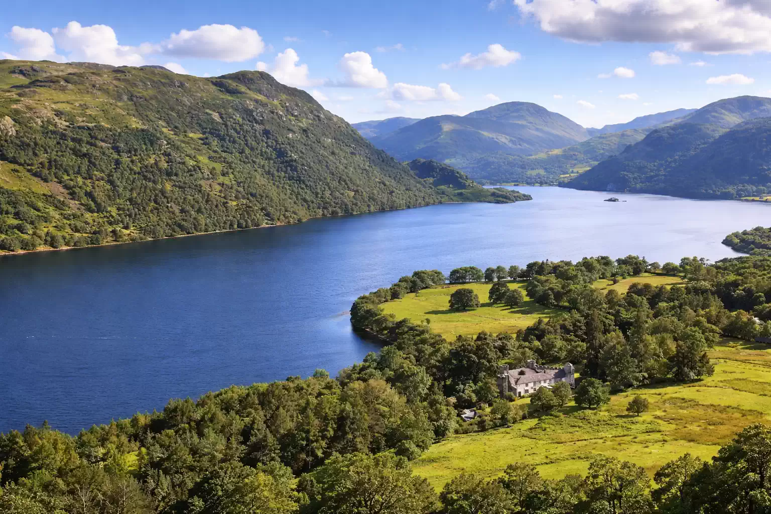 Panoramic view of Ullswater lake surrounded by green mountains and countryside, iconic Lake District landscape in the UK