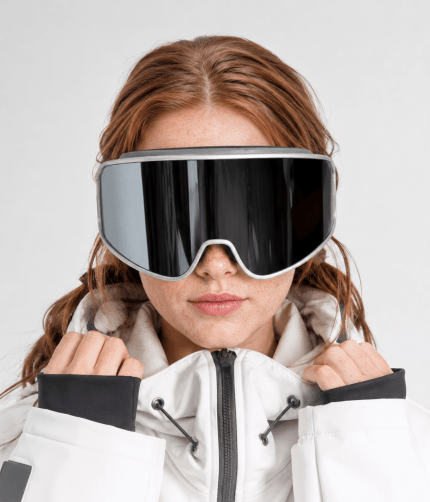 Woman wearing oversized black mirrored ski goggles with a white winter jacket
